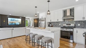 Une cuisine moderne dotée d’un îlot central, de tabourets de bar, d’appareils électroménagers en acier inoxydable et d’une grande fenêtre.