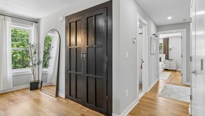 Un couloir avec une grande porte en bois sombre, une plante en pot et un miroir accroché au mur.