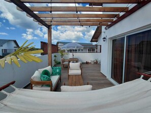 A covered outdoor patio with wooden furniture, a hammock, and a view of a house in the background. - 2 Bedroom Elegant Penthouse 400m from Punta Popy Beach in Las Terrenas (Las Terrenas)