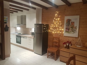 Eine Küche mit Kühlschrank, Holzschränken, einer Spüle und einem Essbereich mit Stuhl und Tisch.
