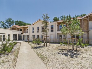 A modern building with multiple balconies, a central pathway, and a sandy ground area. - Twin Fin Apt for 4 - Shared Pool (Biscarrosse)