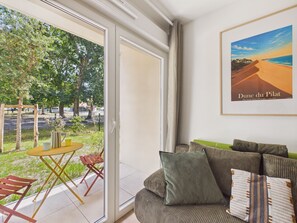A room with a sofa, a table, and a chair, a large window, and a framed picture on the wall. - Twin Fin Apt for 4 - Shared Pool (Biscarrosse)