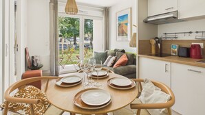 En matplats med ett runt bord för fyra personer, en soffa och ett köksområde med skåp och en hängande lampa.