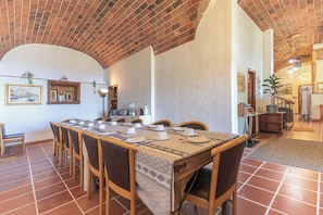 Un comedor con una mesa larga dispuesta para seis personas, rodeada de sillas, con techo de ladrillo y suelo de baldosas.