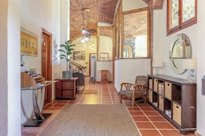Un pasillo con una escalera de madera, un mostrador de recepción, una silla, un aparador con cestas y un espejo.