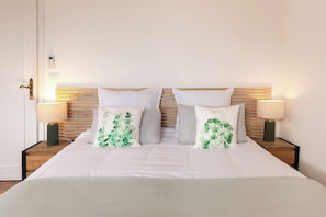 Una cama doble con cabecera de madera, dos lámparas de noche y una planta verde sobre la mesita.