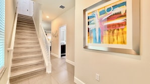 A staircase leading to a second floor, a hallway with a framed abstract painting, and a door at the end of the hallway. - Private Pool, Balcony & BBQ Area Short Walk to Clubhouse (Clermont)