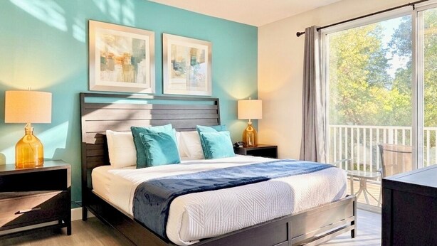 A bedroom with a bed, two bedside tables with lamps, a large window with a view of trees, and two framed pictures on the wall. - Private Pool, Balcony & BBQ Area Short Walk to Clubhouse (Clermont)