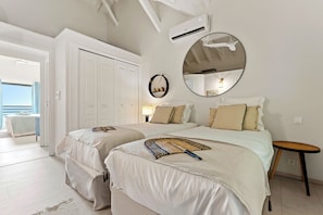 A bedroom with two beds, a ceiling fan, a large mirror, and a window with curtains. - Villa Anse Marcel piscine & jacuzzi (Anse Marcel)