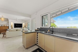 A modern kitchen with a large window, a built-in sink, and a dining area with a sofa and table. - Villa Anse Marcel piscine & jacuzzi (Anse Marcel)