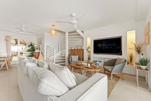A modern living room with a sofa, a coffee table, a TV, and a staircase. - Villa Anse Marcel piscine & jacuzzi (Anse Marcel)