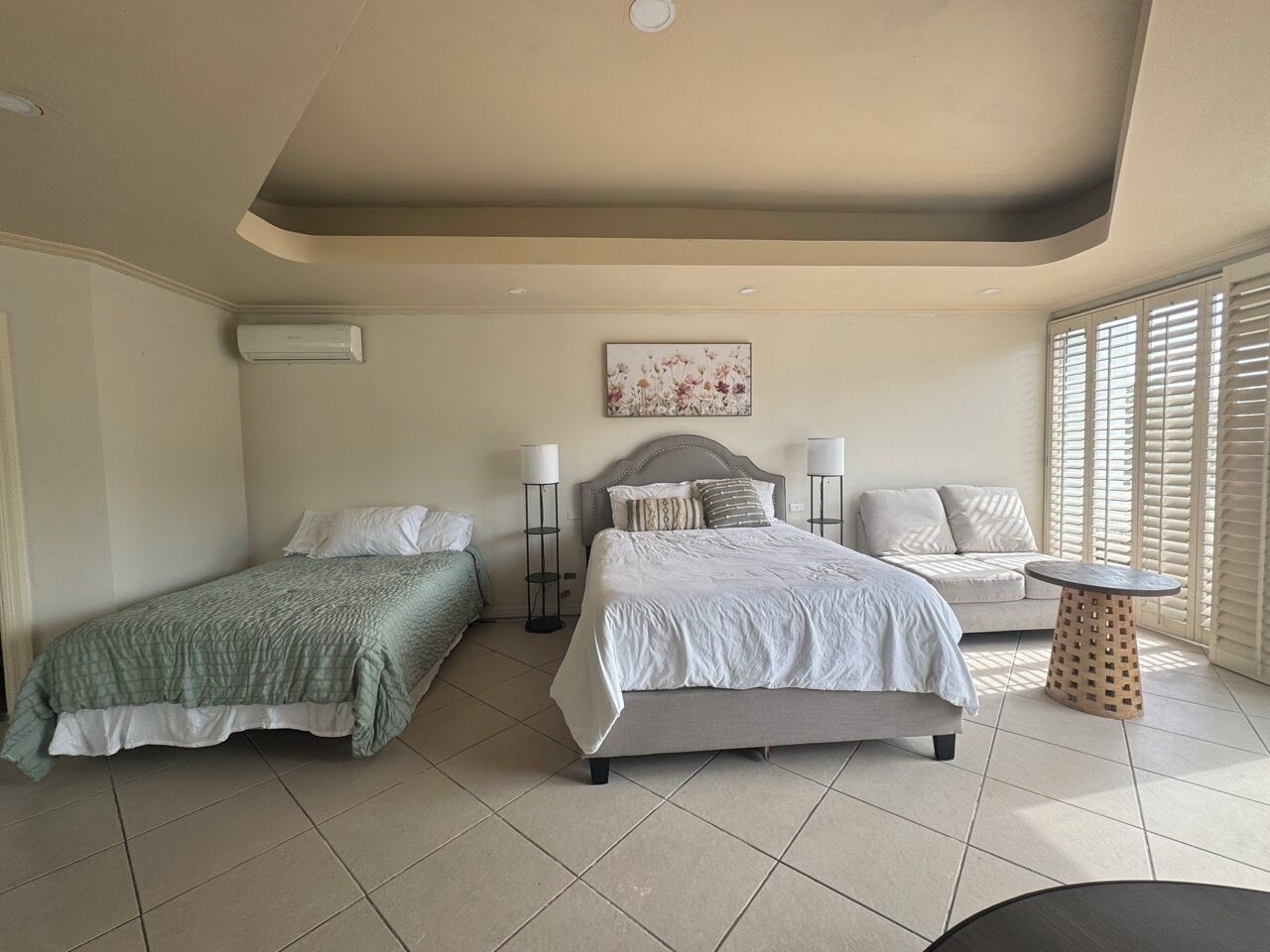 A bedroom with two beds, a sofa, a small round table, and a window with blinds.