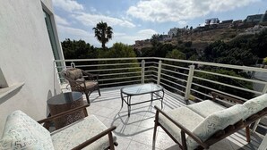 Een balkon met twee loungestoelen, een klein tafeltje en een glazen tafel.