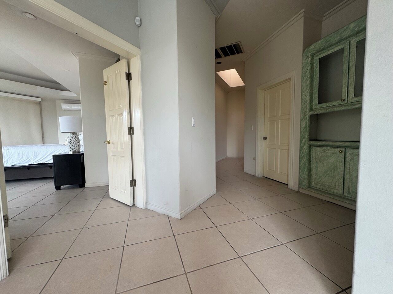A hallway with a bed, a nightstand, and a green cabinet.