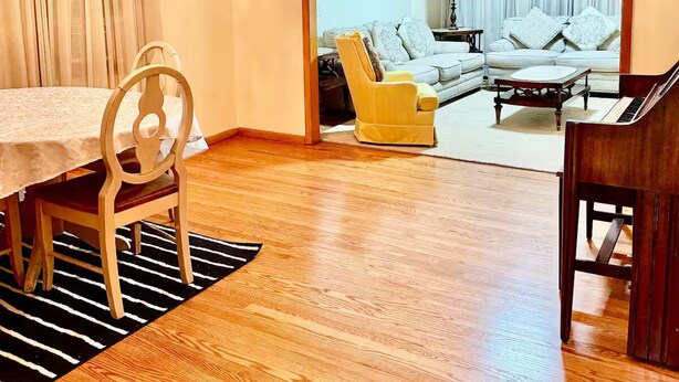 Un vaste espace de vie comprenant une table à manger, un fauteuil jaune, un piano et un lustre.