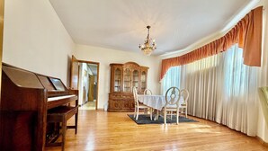Une pièce comprenant un grand piano, une table à manger avec des chaises, un lustre et une grande fenêtre avec des rideaux.
