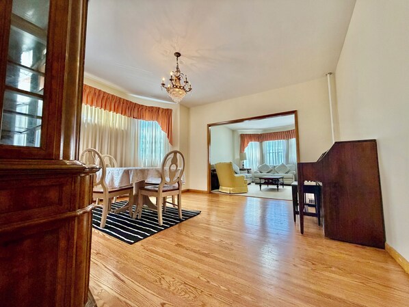 A spacious living room with a dining area, a chandelier, and a large mirror reflecting the room.