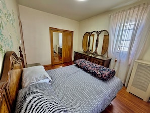 Un dormitorio con cama, cómoda con espejos, armario y radiador.