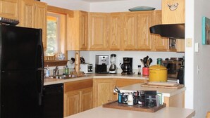 Una cocina con gabinetes de madera, un refrigerador negro, una cafetera y una olla amarilla sobre la encimera.