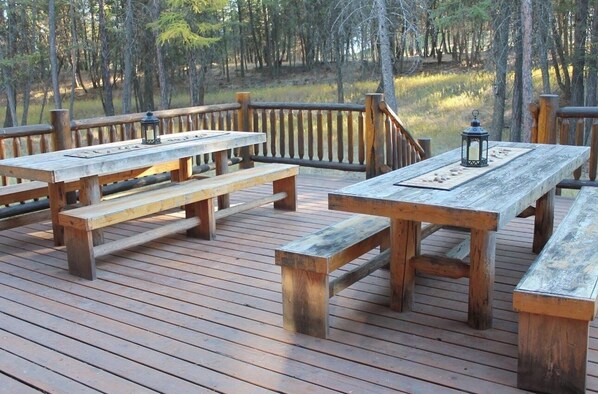 Une terrasse en bois, agrémentée de tables de pique-nique et de bancs, et entourée d’une balustrade en bois.