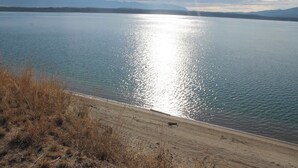Una playa con vista despejada a un lago tranquilo, montañas distantes y un cielo parcialmente nublado.