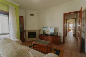 Ein Wohnzimmer mit Kamin, Fernseher, Sofa und einem zur anderen Kammer führenden Flur.