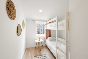 Une chambre avec un lit superposé, une petite table et une lampe, une fenêtre donnant sur des immeubles et des œuvres d’art mural.
