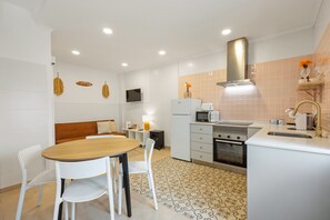 Une cuisine moderne avec des appareils électroménagers blancs, un coin repas avec une table et des chaises en bois, et un téléviseur fixé au mur.