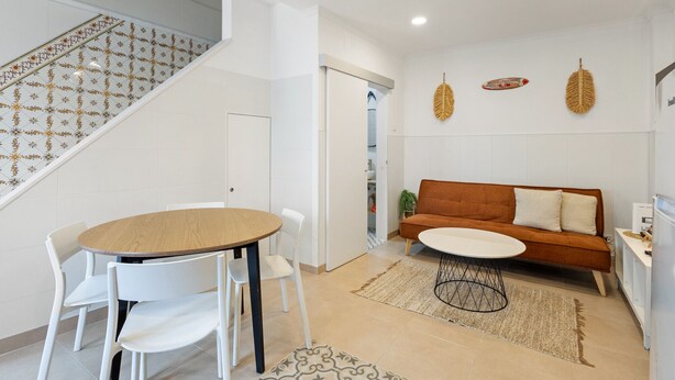 Una sala de estar moderna con una mesa redonda de madera, sillas blancas, un sofá marrón y una alfombra estampada.