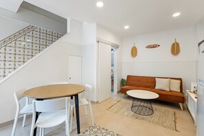 A modern living room with a round wooden table, white chairs, a brown sofa, and a patterned rug.