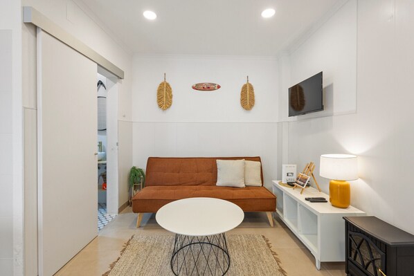 A modern living room with a brown sofa, a white table, and a TV mounted on the wall.