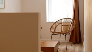 Una habitación con una silla de mimbre, una mesita de madera y una ventana con cortinas.