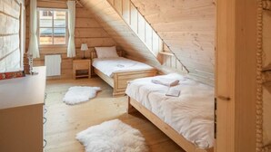 A cozy attic bedroom with wooden walls, two beds, a window with curtains, a bedside table, and a fluffy rug. - Half of a Semi-detached House With a Sauna (Koscielisko)