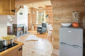 Ein rustikales Blockhaus-Interieur mit Küchenzeile, Kamin, Esstisch und Kühlschrank.