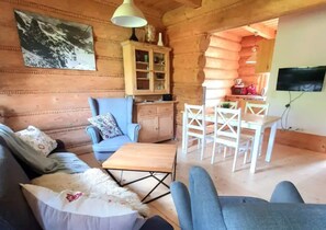 Ein rustikales Blockhaus-Interieur mit einer Couch, einem Sessel, einem Esstisch und Stühlen.