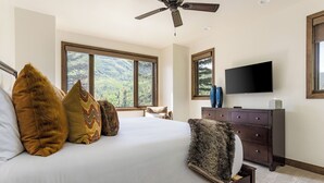 Une chambre dotée d’un grand lit, d’un ventilateur de plafond, d’une télévision et offrant une vue sur l’extérieur par les fenêtres.