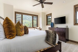 Ein Schlafzimmer mit einem großen Bett, einem Deckenventilator, einem Fernseher und Blick ins Freie durch die Fenster.