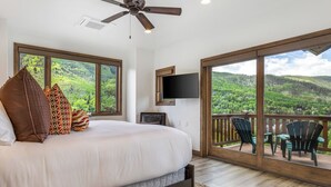 Une chambre avec un grand lit, un ventilateur de plafond, une télévision et un balcon équipé de chaises.