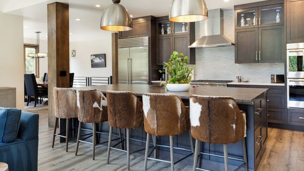 Une cuisine moderne dotée d’un îlot central, de tabourets de bar, d’appareils électroménagers en acier inoxydable et de luminaires suspendus.