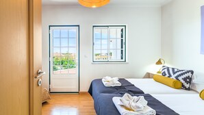 A hotel room with a bed, a window, a door, and a view of greenery outside.