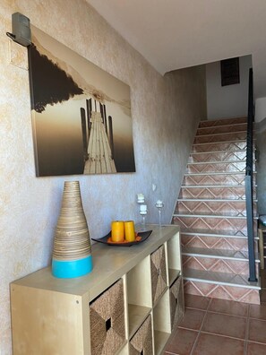 Una escalera con un diseño de azulejos ornamentados, una obra de arte en la pared que muestra un muelle de madera y una consola con un florero y velas.