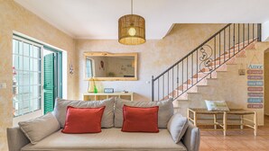 A living room with a sofa, a hanging light fixture, a staircase, and a wall with a mirror and a sign.