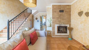 A living room with a staircase, a fireplace, and a kitchen in the background.