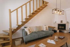 Eine Holztreppe, ein graues Sofa mit Kissen, ein Holztisch und eine Pendelleuchte.
