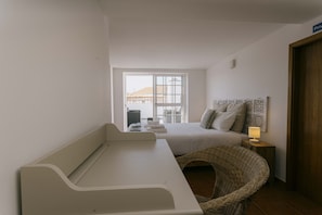 Ein Schlafzimmer mit Bett, Nachttisch, Lampe, Korbsessel und Blick ins Freie.
