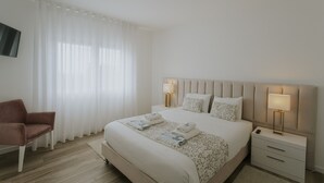 Ein Hotelzimmer mit Bett, Nachttischen, einem Sessel und einem Fernseher.