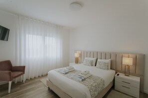 Ein Hotelzimmer mit Bett, Nachttischen, einem Sessel und einem Fernseher.
