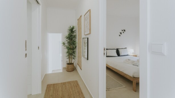 Ein Flur, der in ein Schlafzimmer führt, mit einem Bett, einer Topfpflanze und gerahmten Bildern an der Wand.