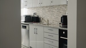 Une cuisine moderne avec des meubles blancs, un four à micro-ondes, une machine à café et un lave-vaisselle.