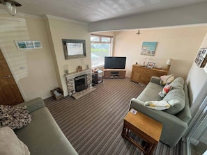 A living room with a fireplace, sofa, television, and a window with blinds.